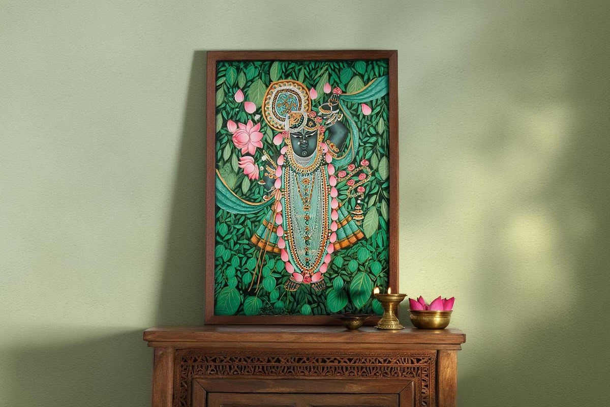 a framed painting of a Hindu deity, surrounded by lush greenery and flowers, placed on a wooden shelf or cabinet.