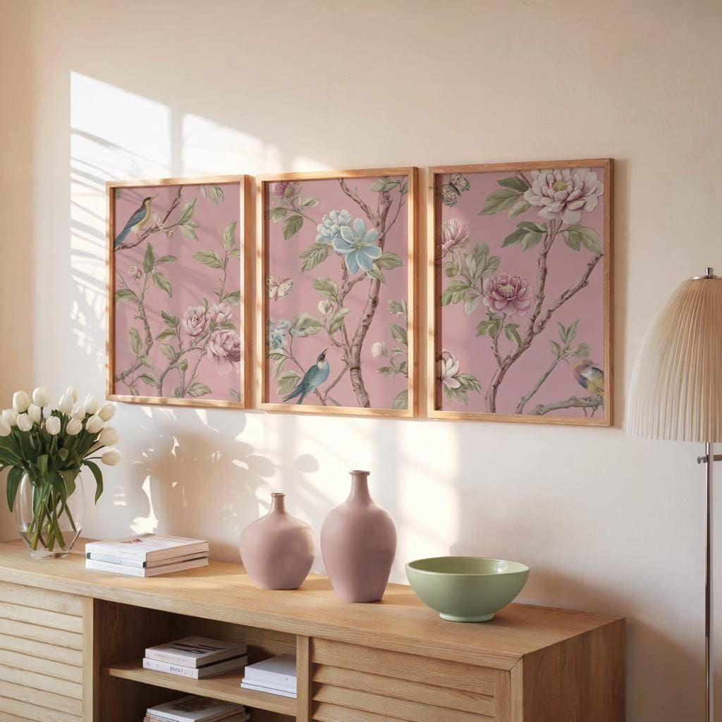a wooden cabinet with three framed floral paintings hanging on the wall above it. The paintings depict various flowers and birds, creating a harmonious and visually appealing display. The cabinet also contains a vase, a bowl, and some books, adding to the overall aesthetic of the room.