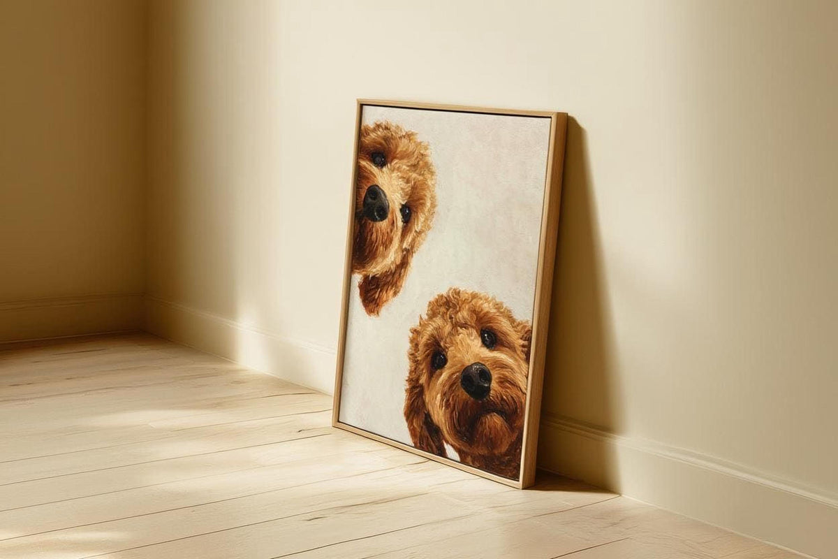 A framed painting of two brown dogs peeking out from behind a wooden frame is leaning against a wall in a room with a wooden floor.