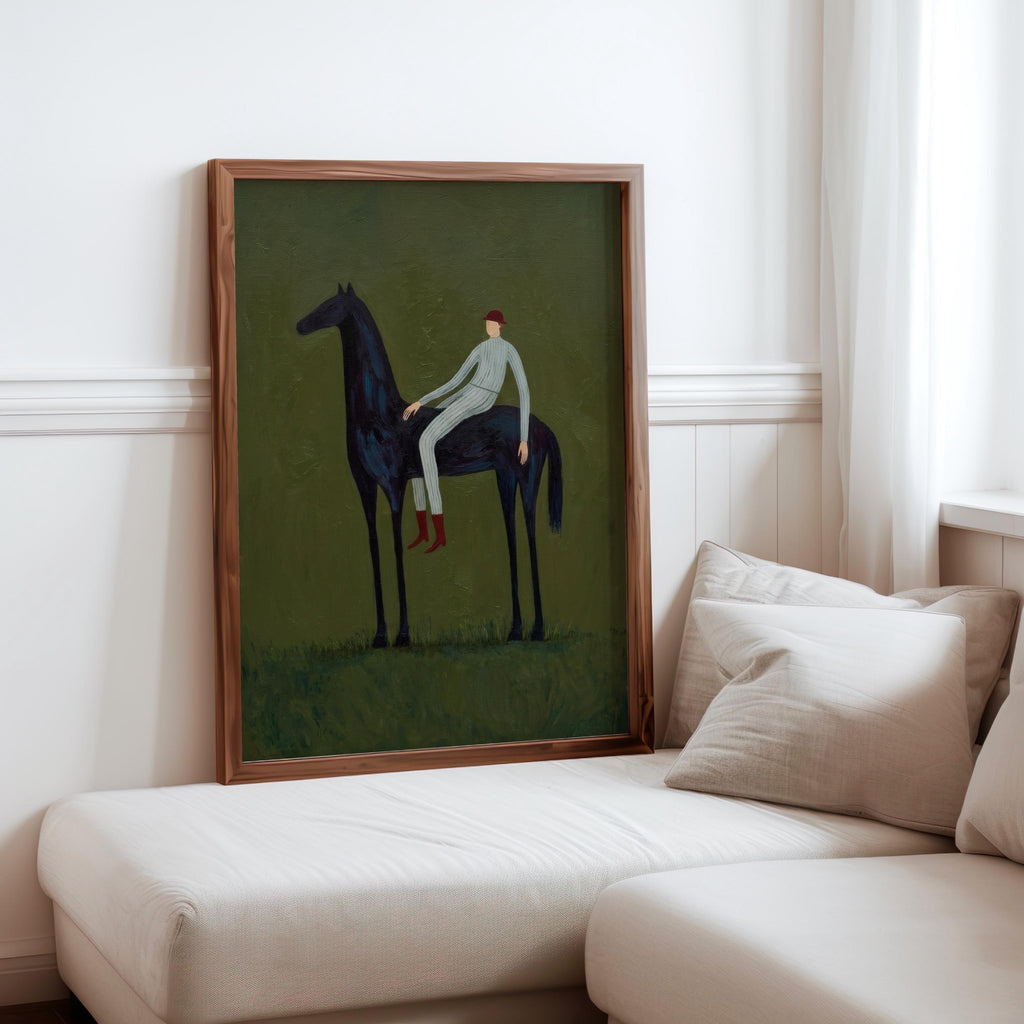 Framed vintage equestrian wall art displayed on living room sofa, slim wood frame, olive green tones.