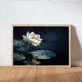 Framed print leaning on light wood floor, luminous white lotus over deep navy pond, white lotus wall art for moody spaces