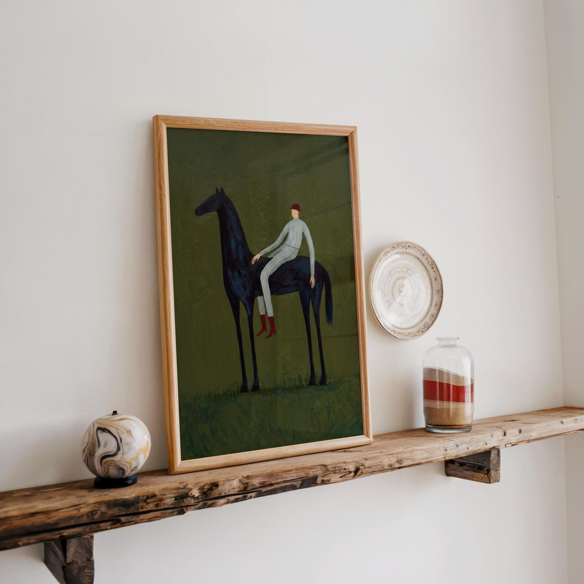 Figurative horse artwork on rustic shelf, slim wood frame against cream wall, small ceramic accents nearby.