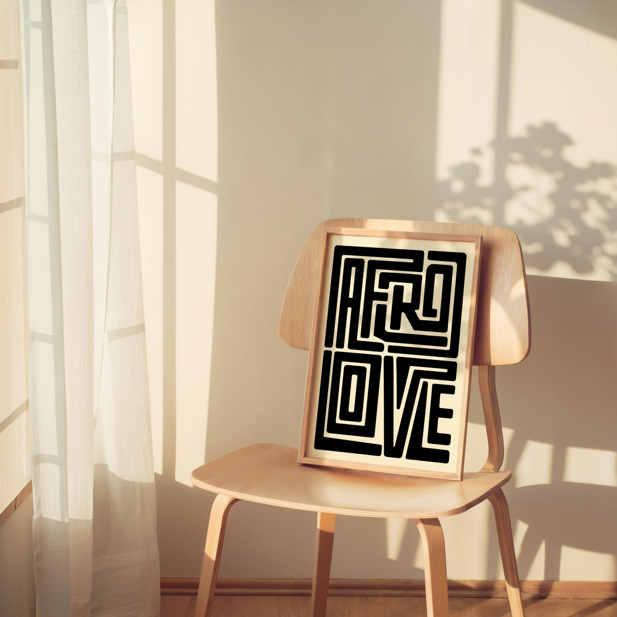 Smaller Afro Love wall art frame placed on woven chair, soft shadows, geometric lettering print in neutral room