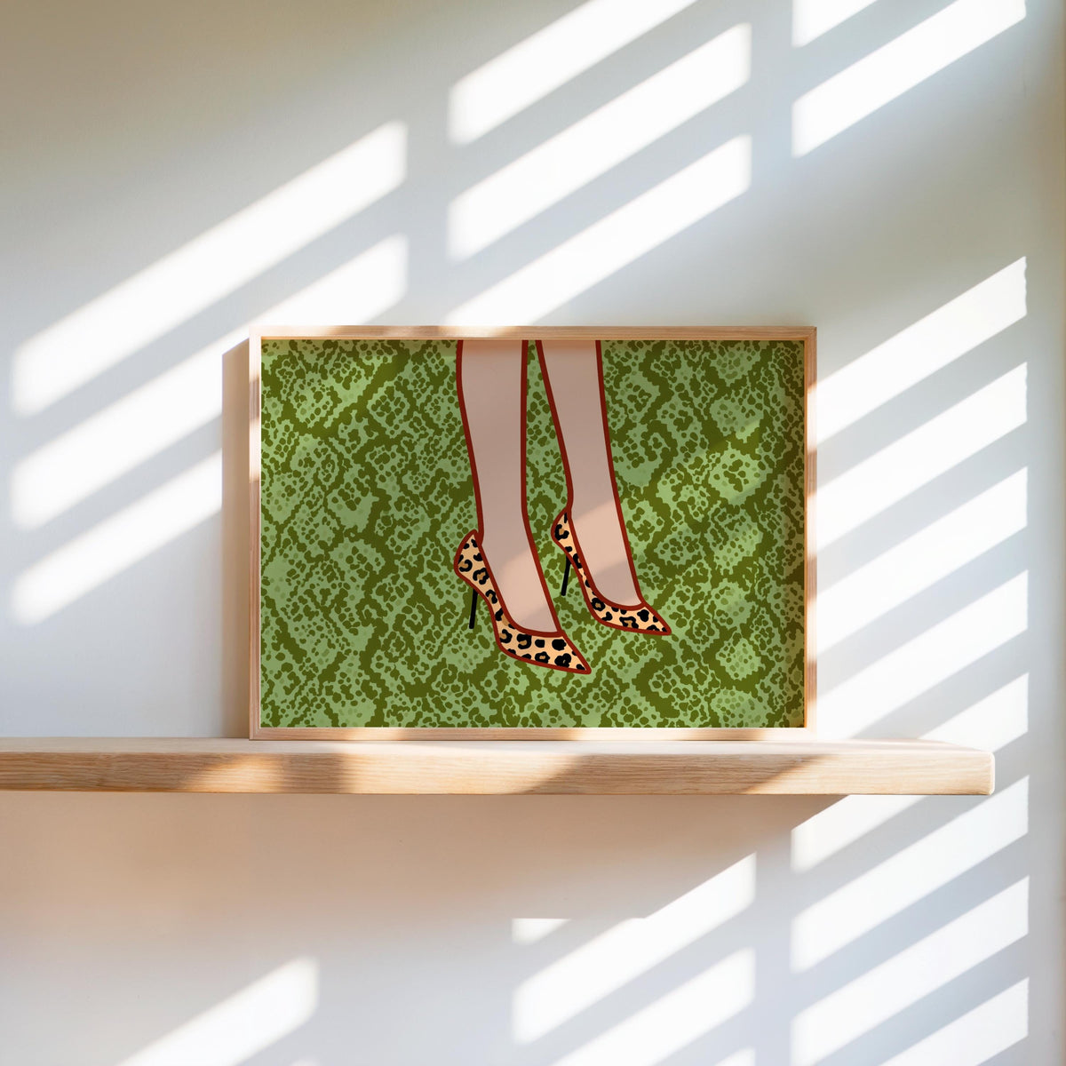 Sunlit shelf vignette with framed leopard print heels wall art, slanted light on green snake-print, chic feminine pumps