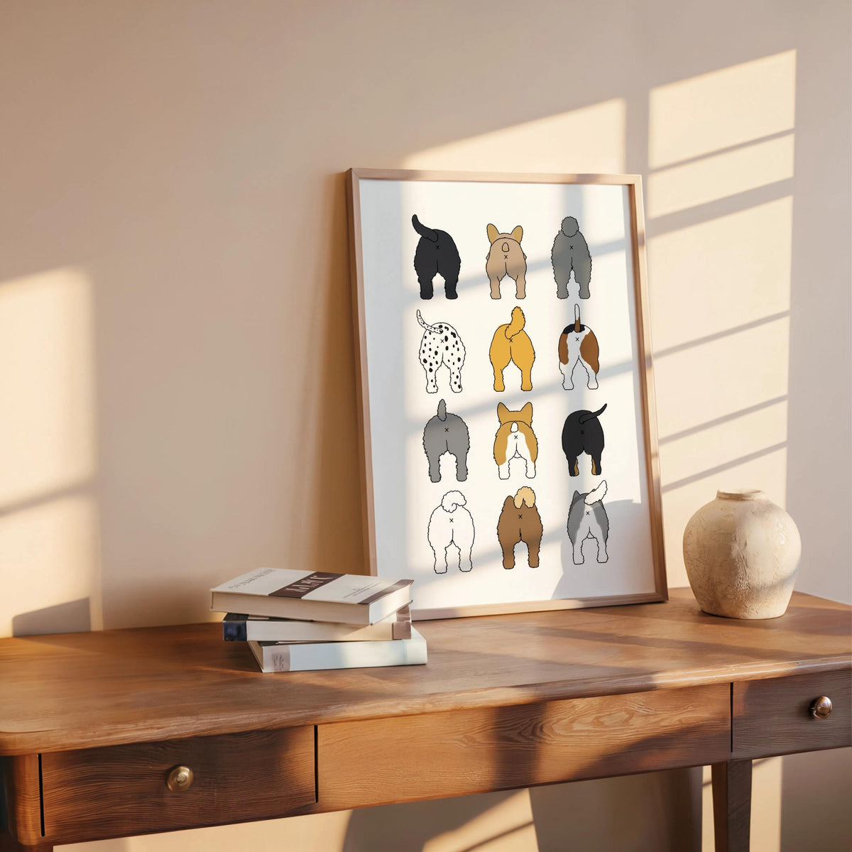Sunlit wooden console holds propped framed print with books and clay pot, playful dog butts wall art for bathroom
