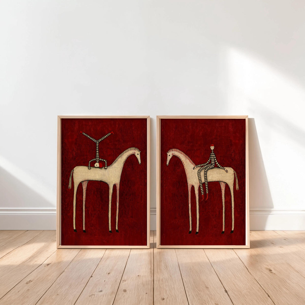 May include: Two framed art prints featuring a deep red textured background. The left print shows a figure in a black and white striped outfit doing a handstand on a white horse. The right print shows a figure in a striped outfit sitting on a white horse.