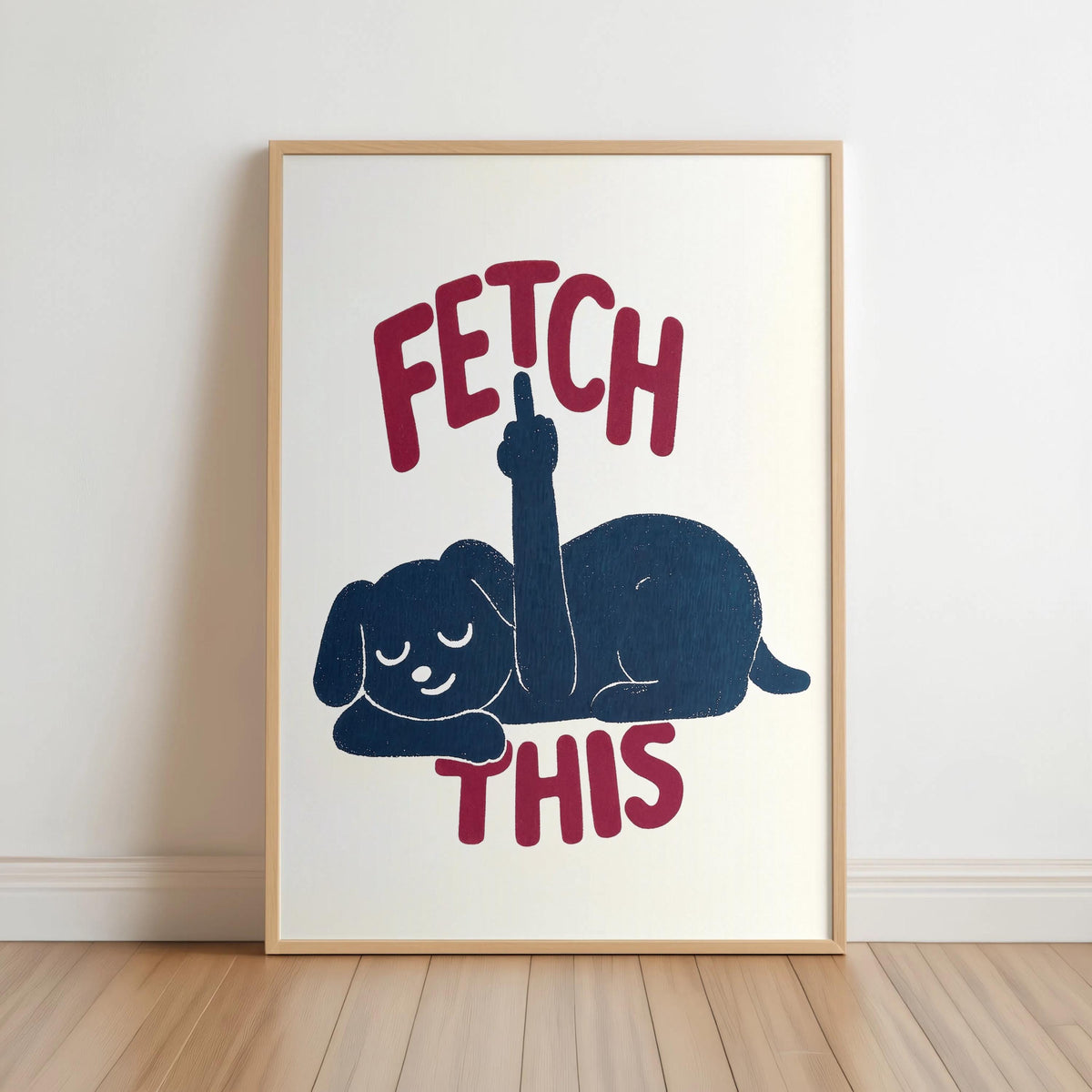 Framed cream print leaning on floor, dark navy dog silhouette with rust-red FETCH THIS lettering, funny dog wall art