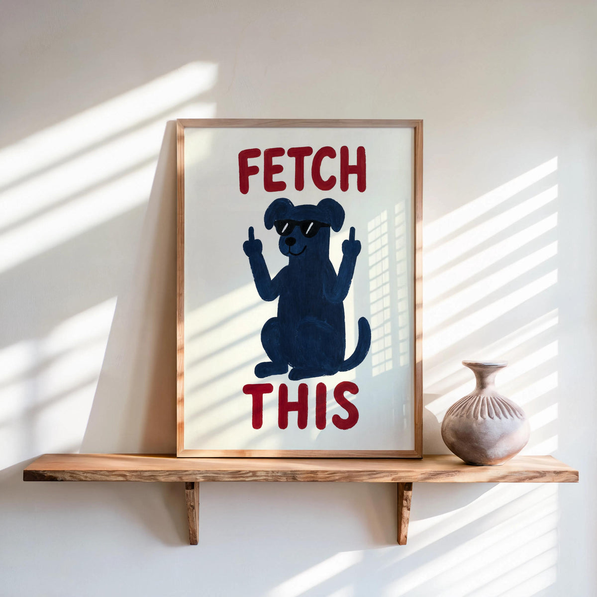 Framed navy dog poster on wall shelf, rust red lettering reads FETCH THIS, retro color palette, funny dog print for sill