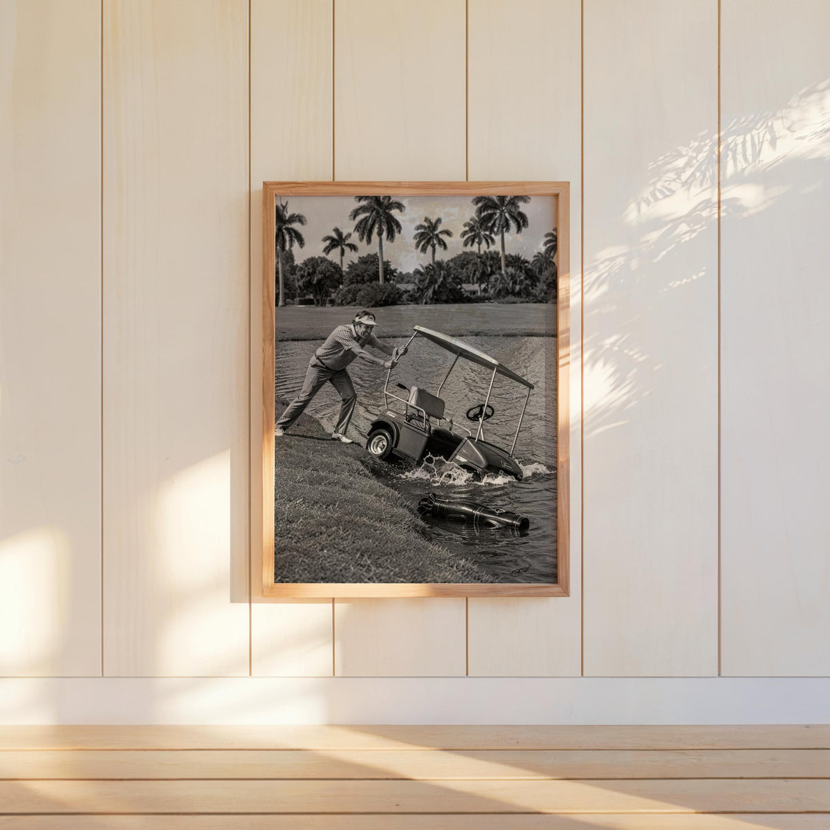 Angry golfer poster hung on white paneled wall, sunlit vintage golf scene in a wood frame.