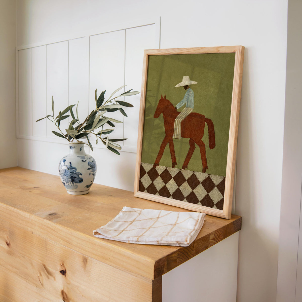 Print leaning on a wooden console with vase and book, folk art cowboy print, ranch wall decor styling suggestion