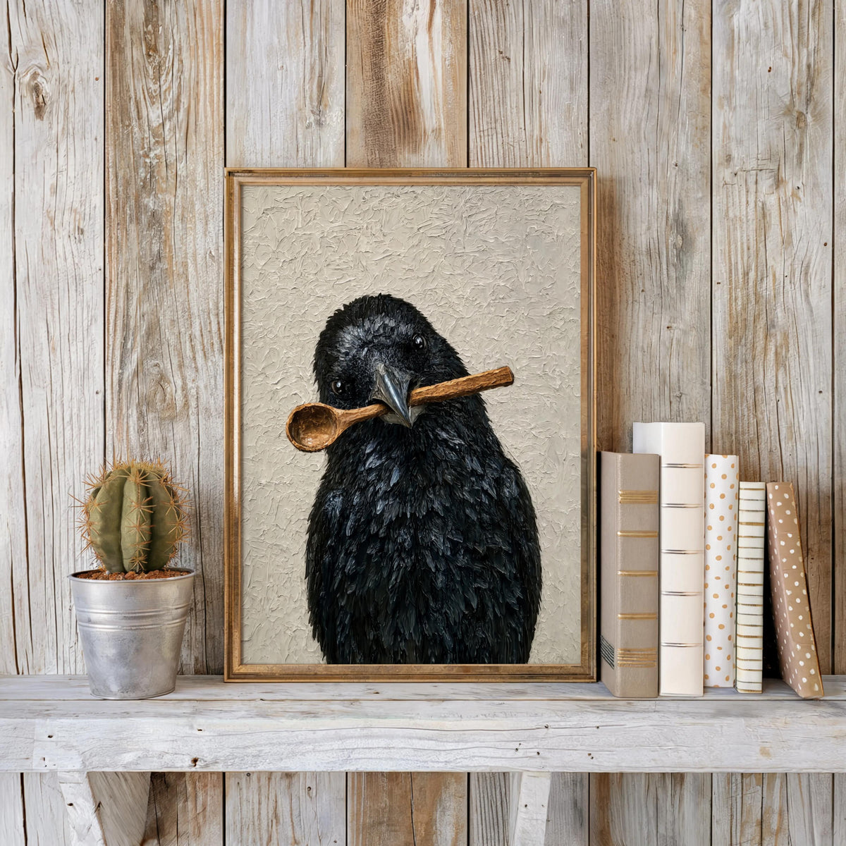 Framed funny crow wall art styled on weathered wood ledge, small cactus and stacked books beside it