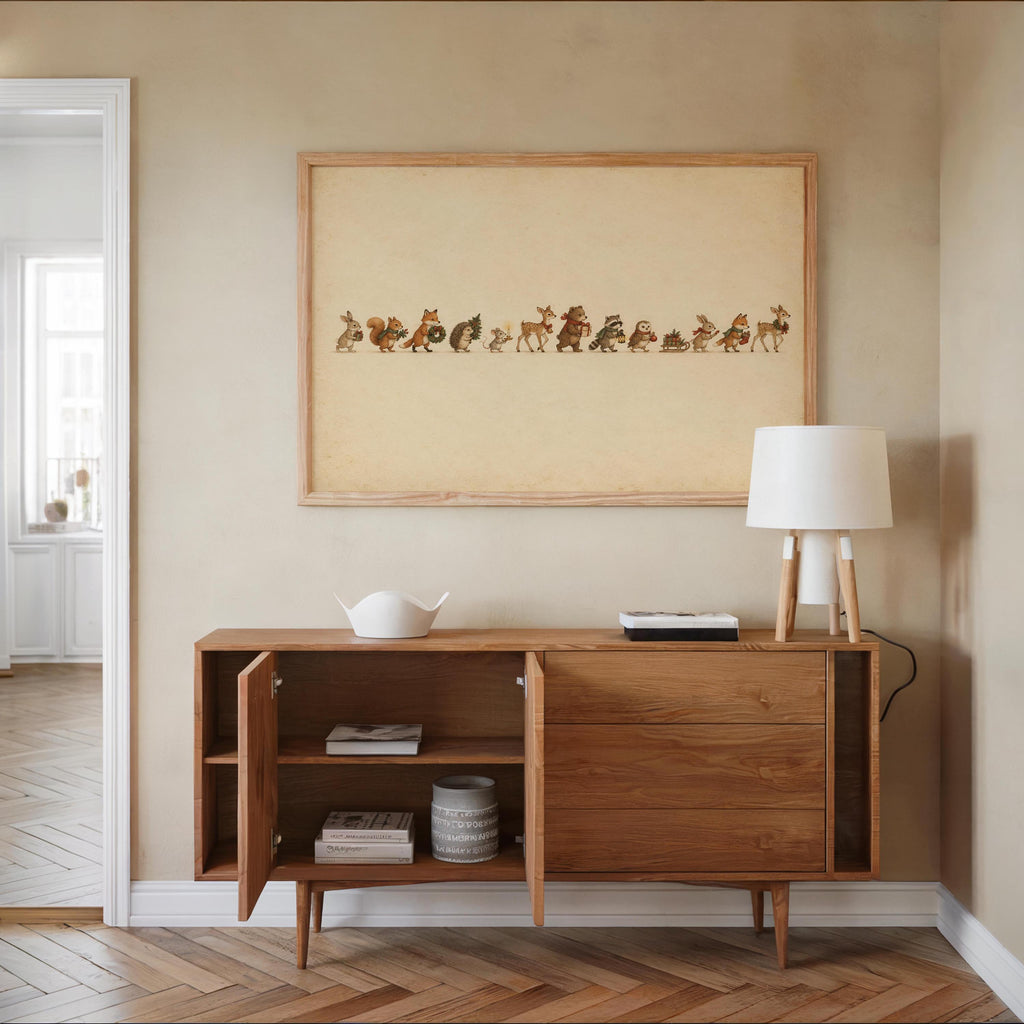 Woodland animal Christmas print centered above a wooden sideboard, lamp, bowl, warm neutral decor