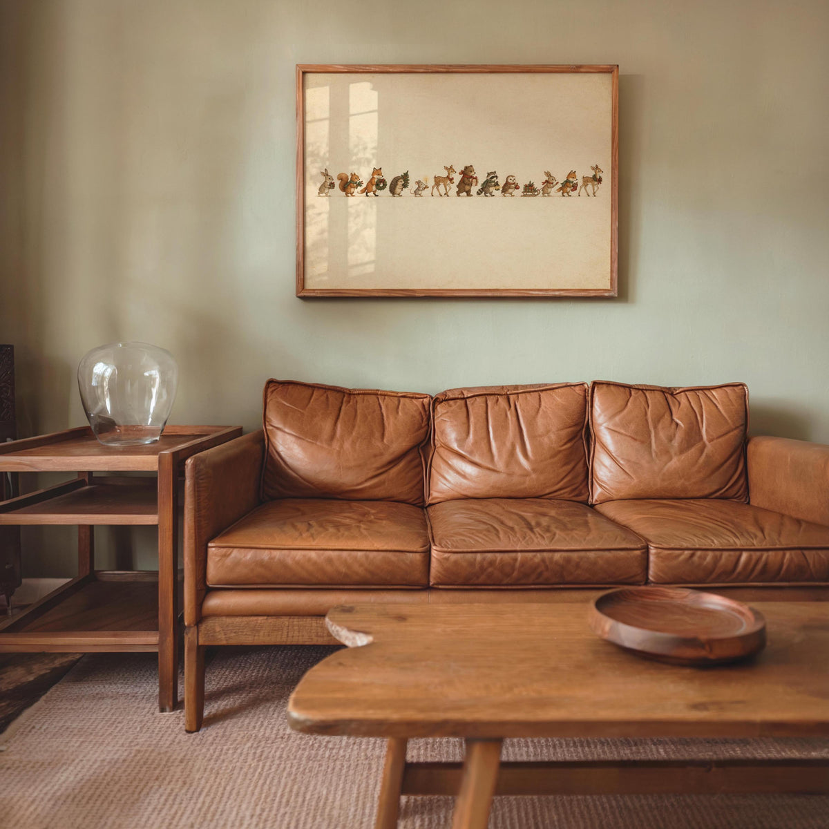 Small framed woodland animal Christmas print over a leather sofa, cozy living room vignette, side table