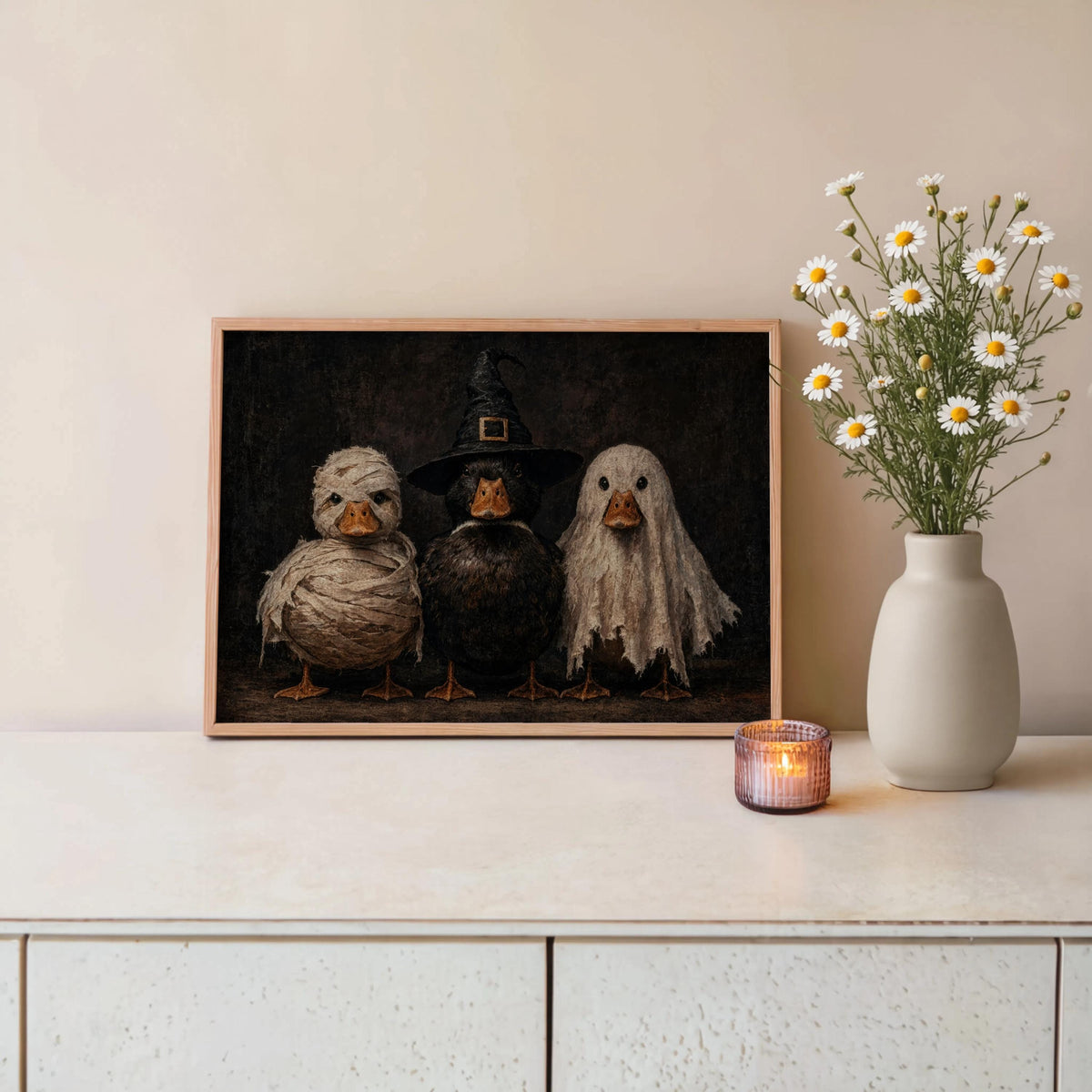 Halloween duck wall art leaning on a console table beside a vase of flowers and candle, duckling Halloween decor, soft cream tones