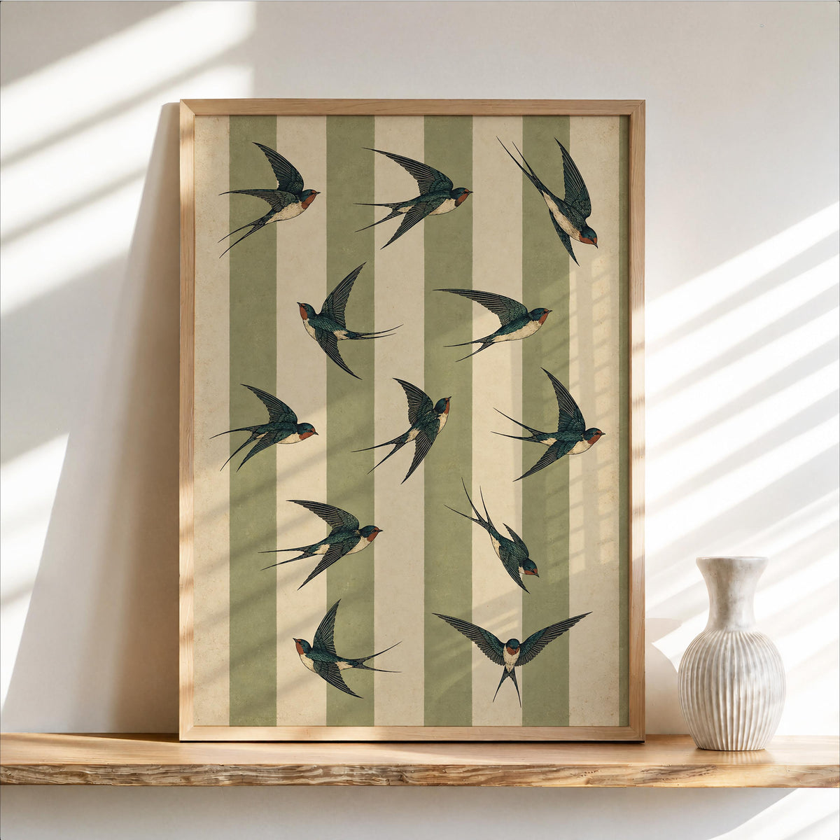 Framed swallow bird wall art leaning on a light wood shelf, sage green striped bird print, retro cottagecore decor