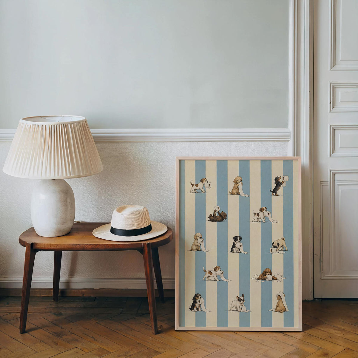 Small framed poster propped by lamp and hat, playful puppies on blue stripes, funny dog bathroom wall art