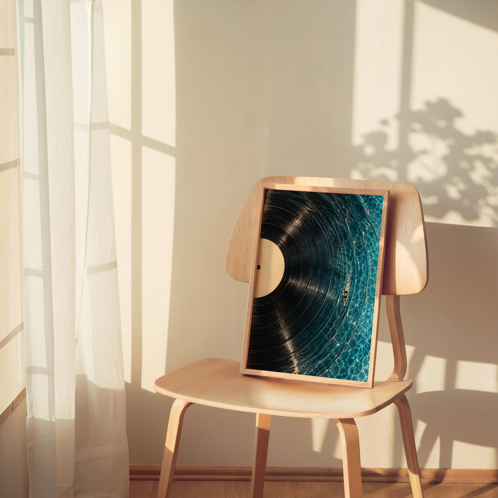 Framed vinyl record wall art perched on a chair by a sunlit window, soft shadows, poolside art print mood
